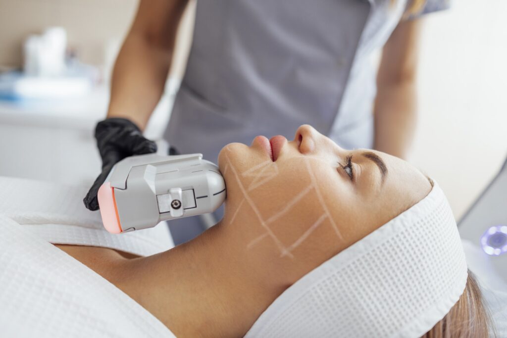 Portrait of relaxed young female client getting SMAS ultrasound face lifting massage