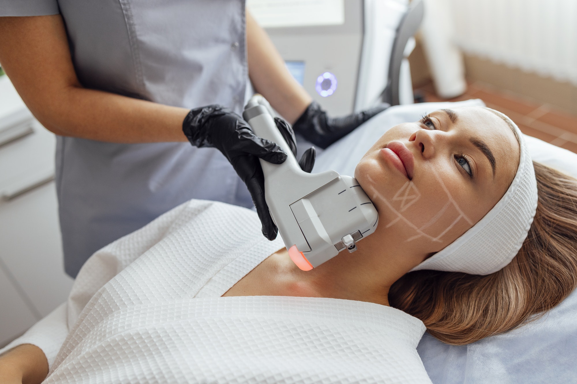 Portrait of relaxed young female client getting SMAS ultrasound face lifting massage