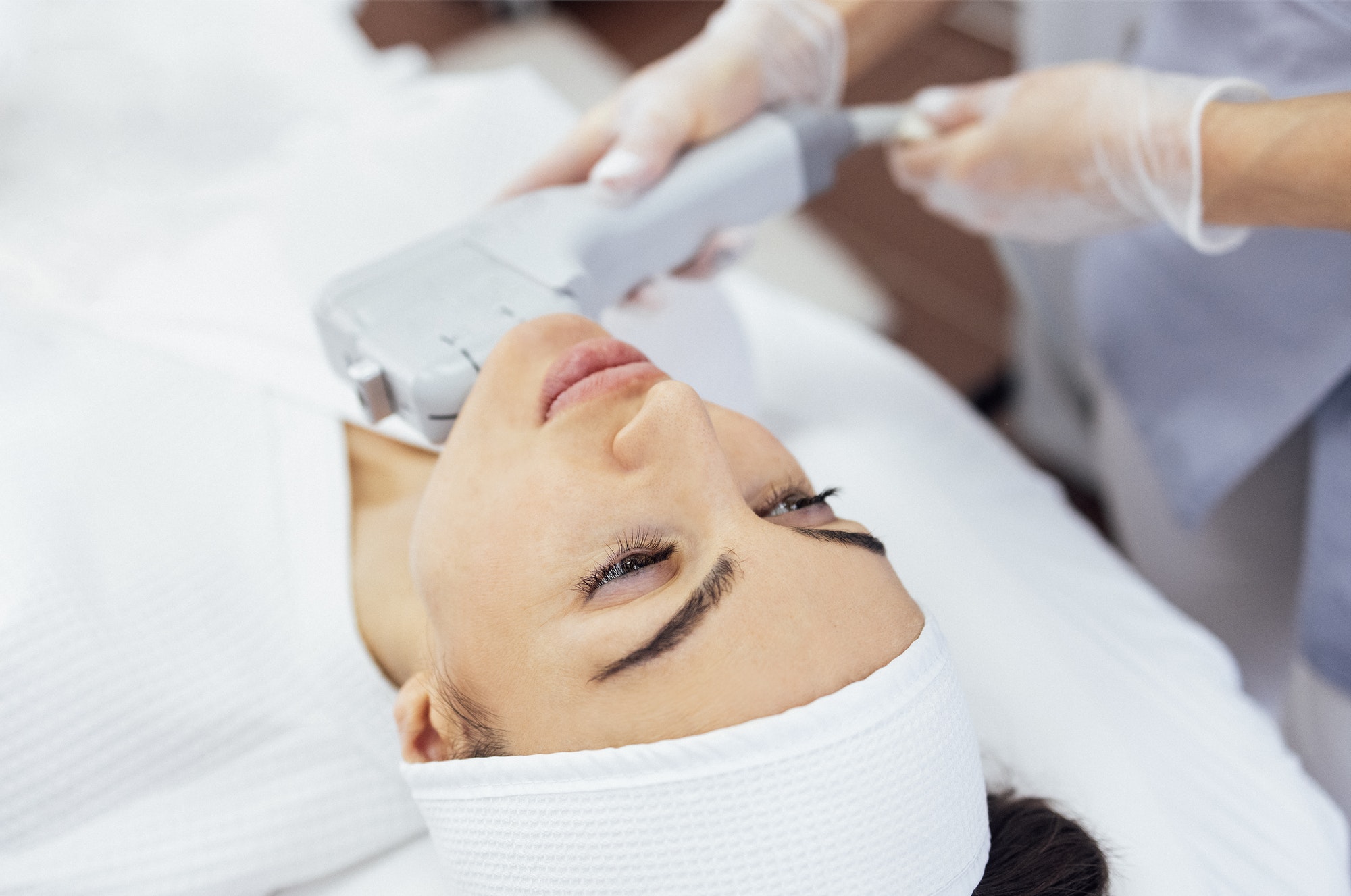 Portrait of relaxed young female client getting SMAS ultrasound face lifting massage